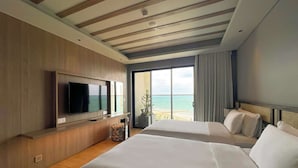 Habitación de hotel con dos camas, un televisor y un amplio ventanal con vista a la playa.