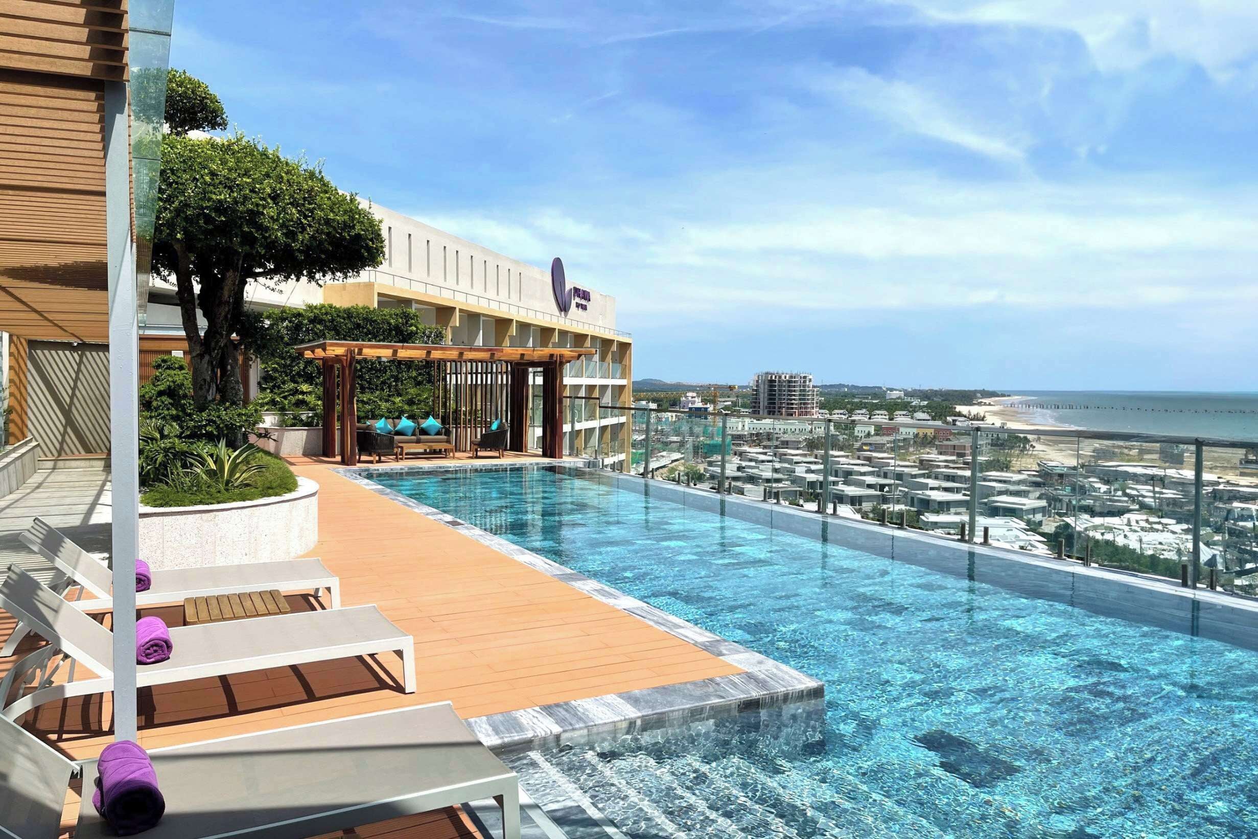 A rooftop infinity pool with lounge chairs and a view of the beach and cityscape.