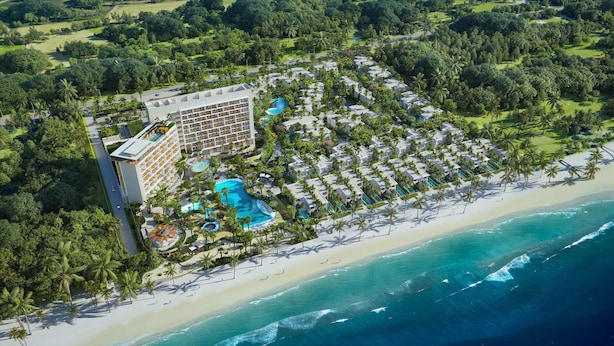 Vista aérea de un complejo turístico con varias edificaciones, una amplia zona de piscina y acceso a la playa.
