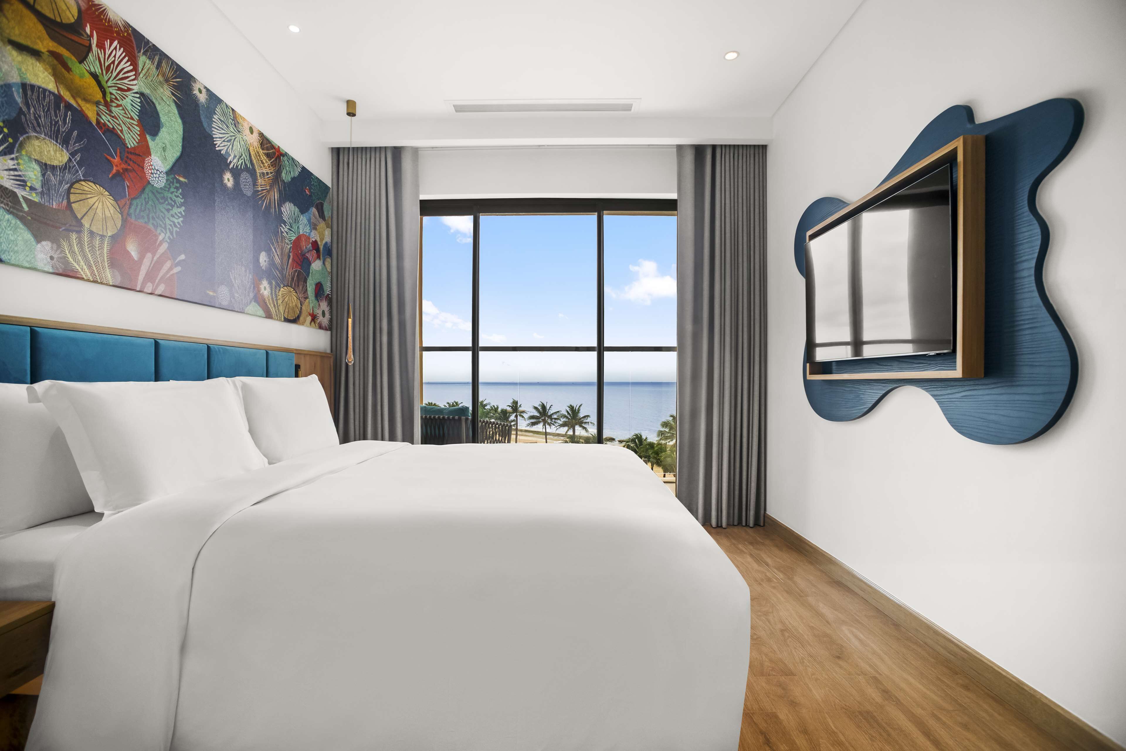 Una habitación de hotel moderna con una cama grande, vista al océano y una obra de arte original en la pared.