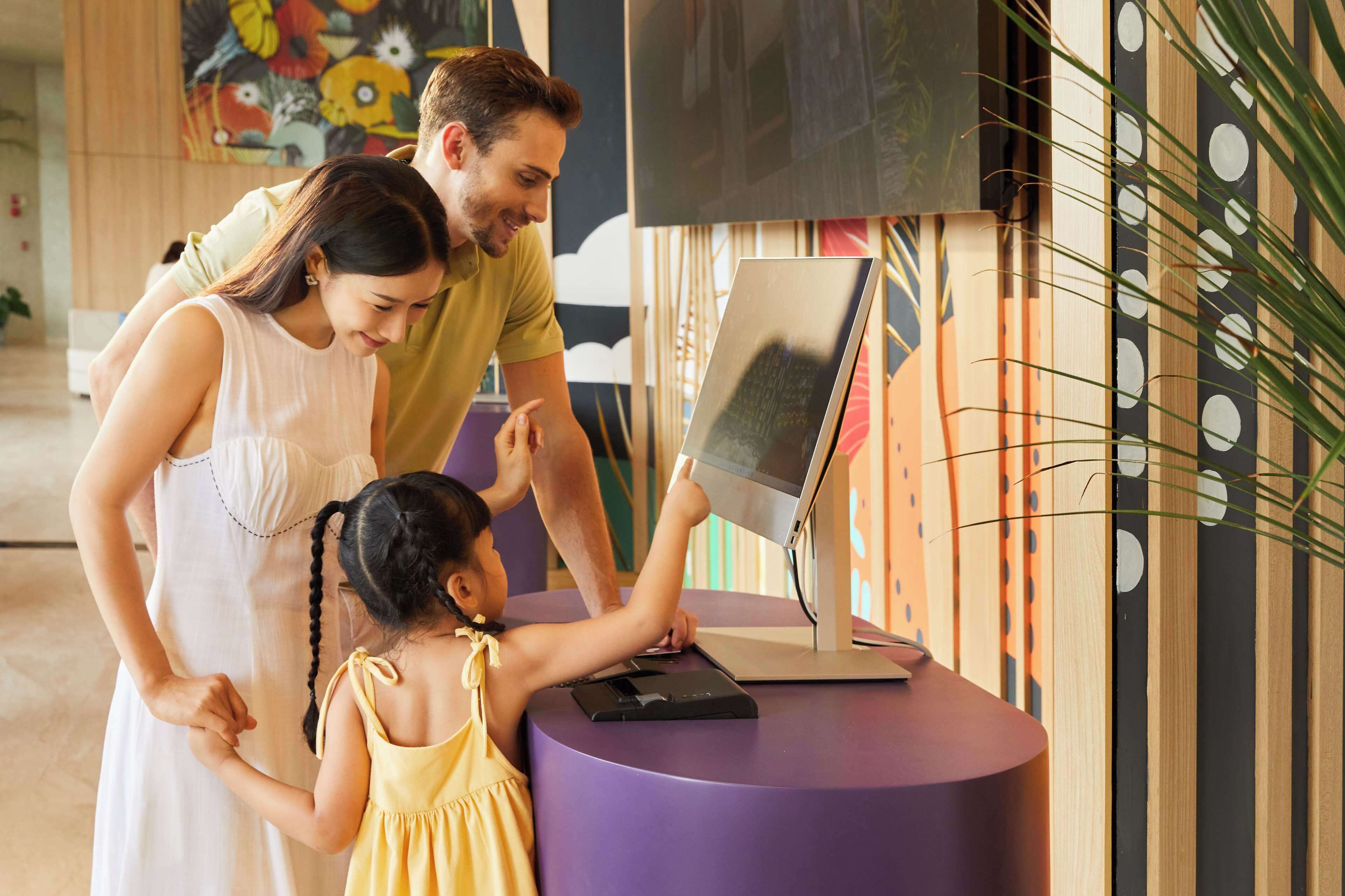 Una familia interactuando con un quiosco digital en un espacio interior moderno, bien iluminado y con decoraciones artísticas en las paredes.