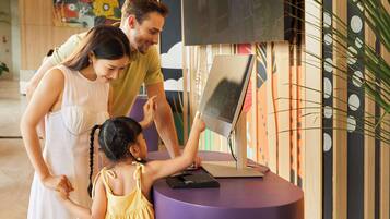 Una familia interactuando con un quiosco digital en un espacio interior moderno, bien iluminado y con decoraciones artísticas en las paredes.