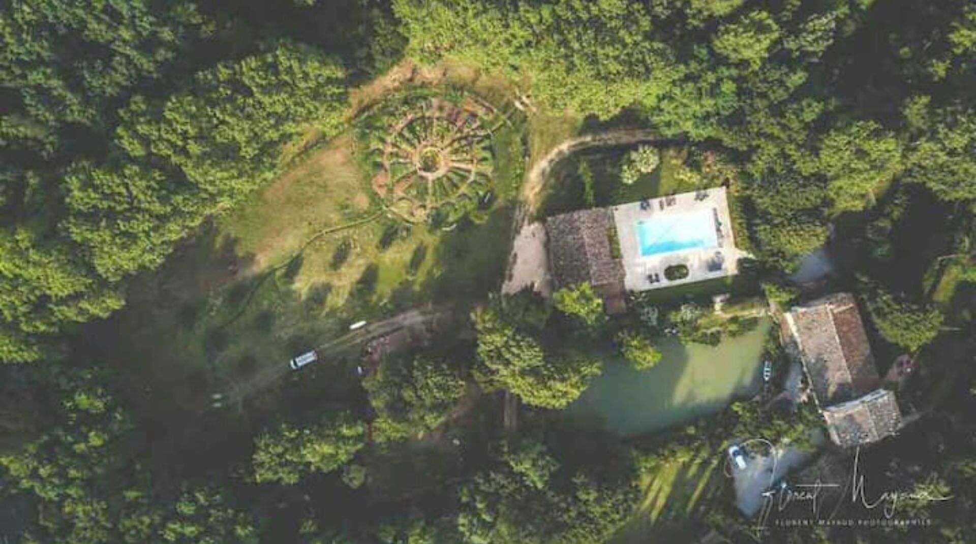 Vista aérea de una propiedad con piscina, jardín circular y un edificio pequeño.