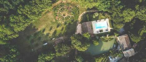Vista aérea de una propiedad con piscina, jardín circular y un edificio pequeño.