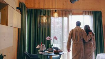 Interior de una cabaña de madera con una mesa para dos, un jarrón de flores y vistas al exterior a través de una ventana.
