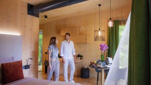 A modern bedroom with a large bed, a wooden ceiling, and a visible kitchen area with wooden cabinets. - Treelodgy (Riva del Garda)