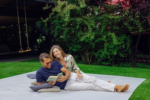 A couple sitting on a large outdoor mat in a garden with lush greenery and a swing in the background. - Treelodgy (Riva del Garda)