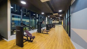 Ein modernes Fitnessstudio mit Holzboden, Trainingsgeräten und großen Fenstern mit Blick auf die Stadt.