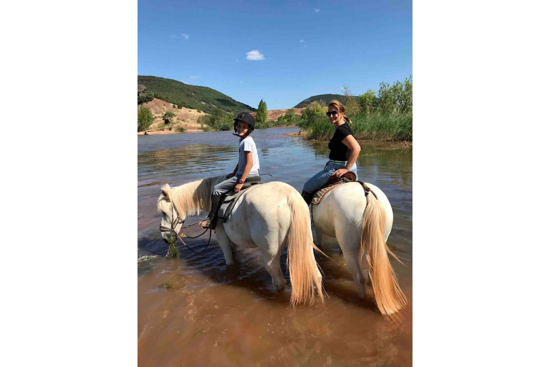 Two people riding horses through a river.