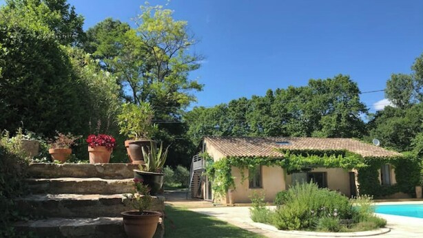 Una scala in pietra conduce a una casa con tetto in tegole, circondata da vegetazione lussureggiante e una piscina.
