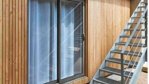 Un edificio moderno con pannelli di legno, un'ampia porta scorrevole in vetro e una scala in metallo.