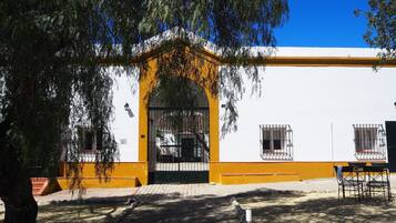 A building with a yellow and white facade, a black gate, and a small balcony with a chair.