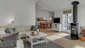 Una sala de estar moderna con un sofá blanco, una mesa de centro con revistas, una chimenea y un comedor al fondo.