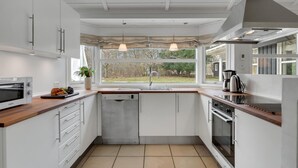 Una cocina moderna con armarios blancos, horno empotrado, lavavajillas y ventana con vistas al exterior.