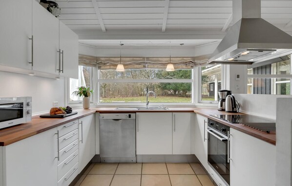 Una cocina moderna con armarios blancos, horno empotrado, lavavajillas y ventana con vistas al exterior.