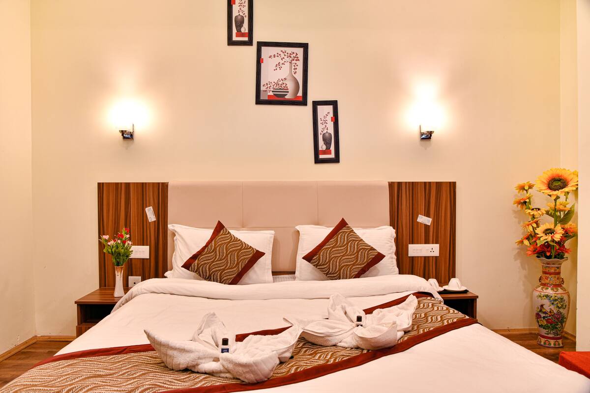 A hotel room with a bed, pillows, a vase with flowers, and wall-mounted lights.