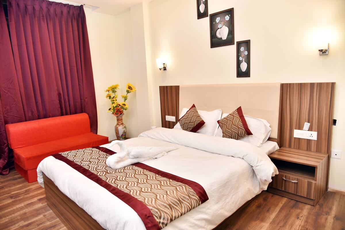 A hotel room with a large bed, a red sofa, a nightstand, and wall-mounted artwork.