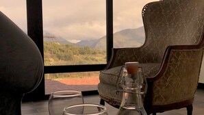 A room with a view of mountains, a chair, and a table with glasses and a bottle.