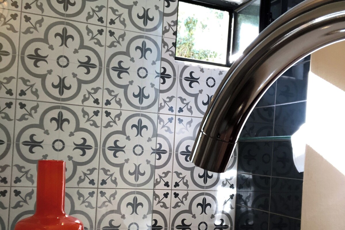A bathroom with a white sink, a red bottle, and patterned tiles.