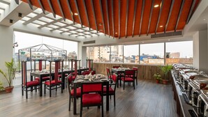 A modern restaurant with wooden ceiling beams, large windows offering city views, and red upholstered chairs. - Hotel Lo Mustang (Kathmandu)