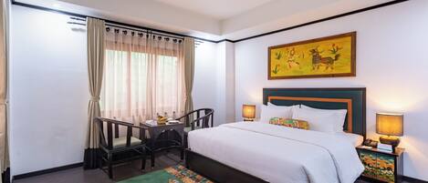 A hotel room with a bed, a desk, a chair, a nightstand, and a window with curtains.