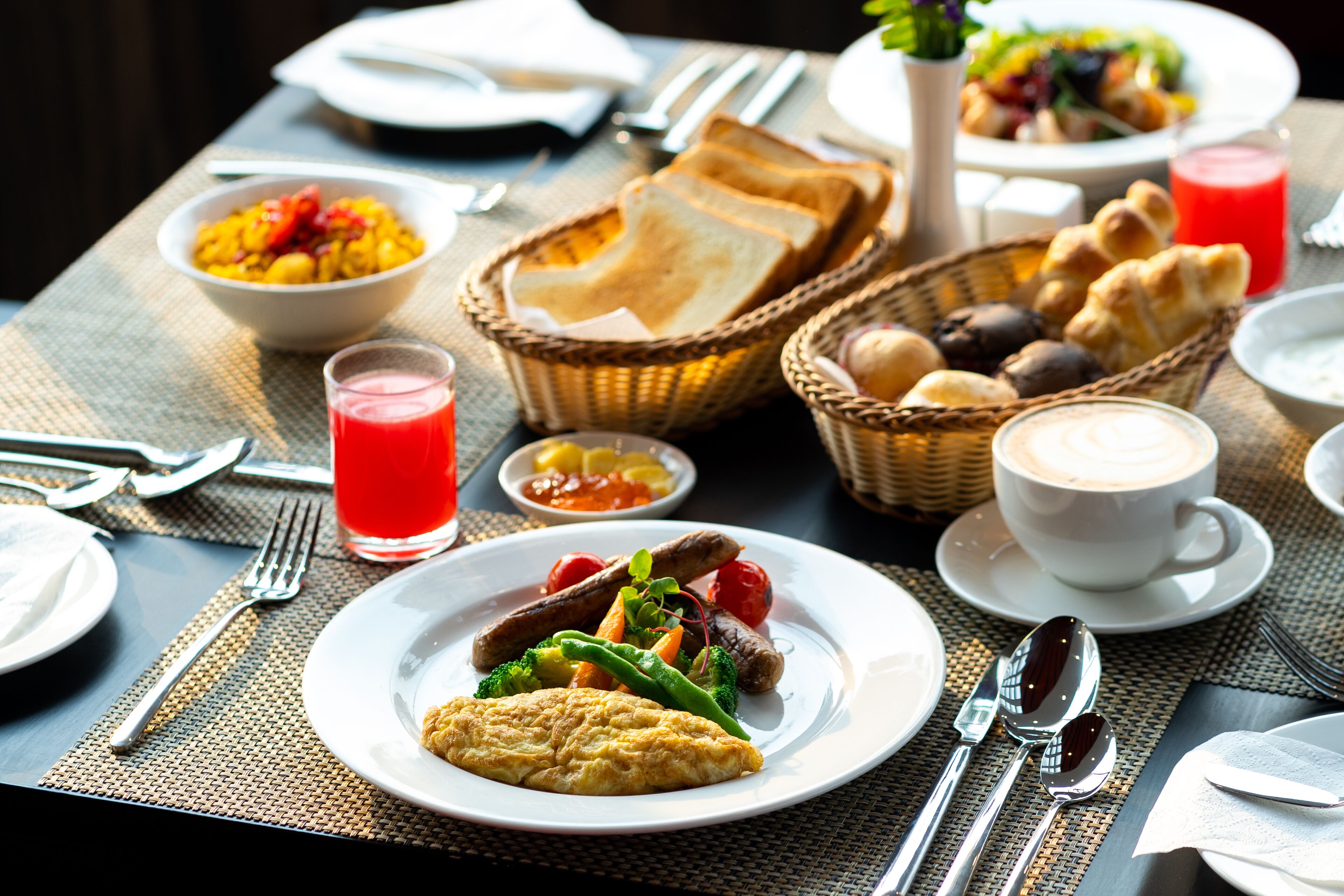 A breakfast setting with plates of food, including eggs, sausages, and vegetables, and a cup of coffee.