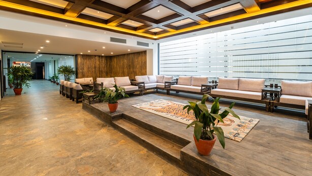 A spacious lobby with a long sofa, a patterned rug, and potted plants. - Hotel Lo Mustang (Kathmandu)