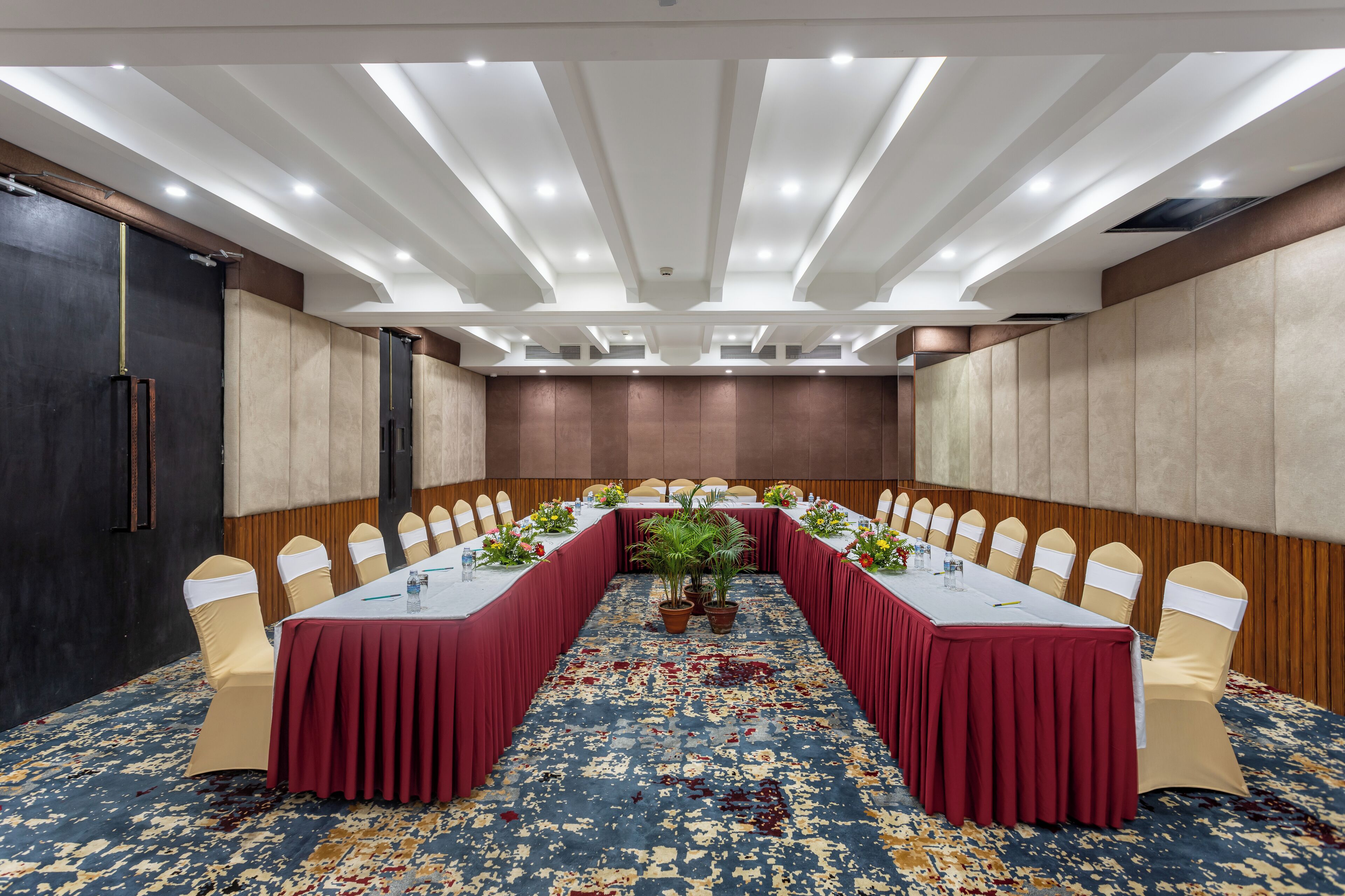 Une salle de conférence avec une longue table, des chaises beiges et une nappe rouge.