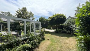 Un jardín con una estructura de vidrio, césped y varios árboles.
