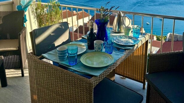 Una terrassa amb moble de vimet, una taula preparada per a dues persones i vista al mar.