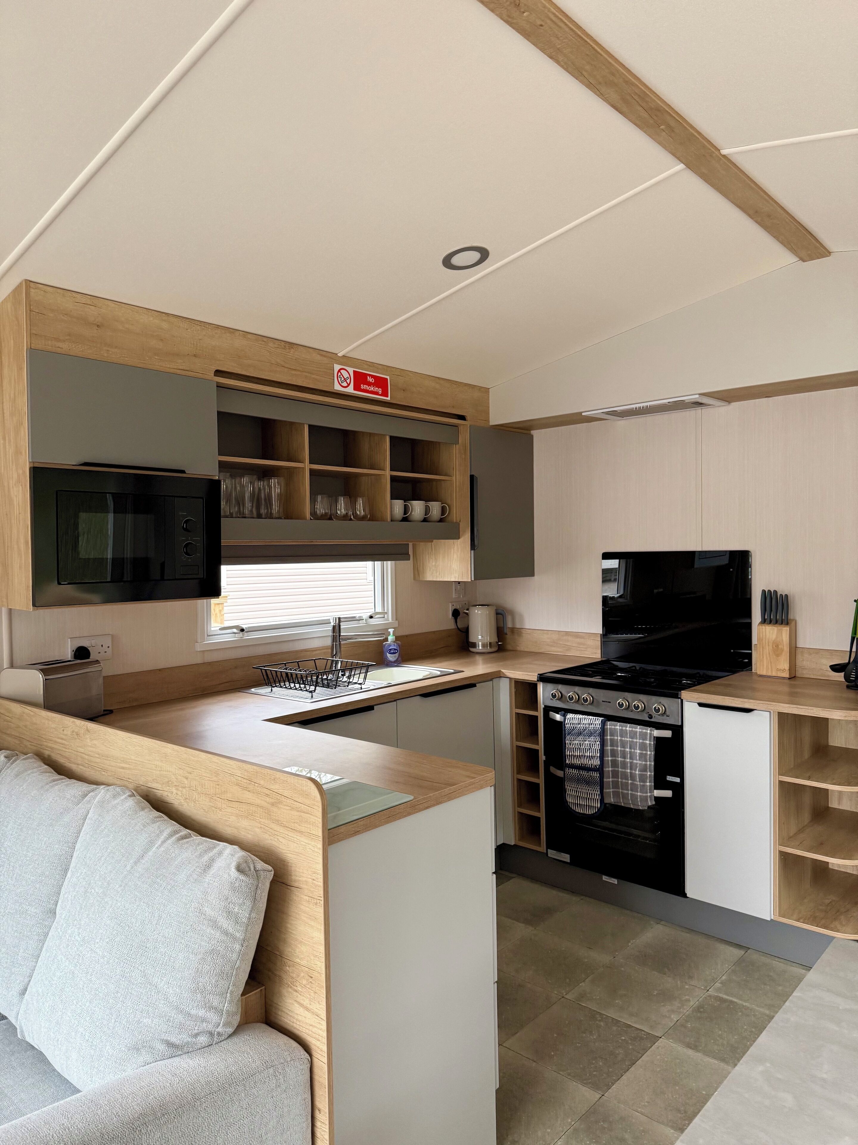 A compact kitchen with a microwave, stove, and sink, wooden cabinets, and a 'No Smoking' sign.
