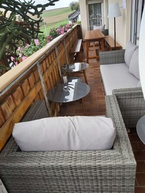 Relax in this serene outdoor seating area with a sofa and two tables, surrounded by a fence and a beautiful view.
