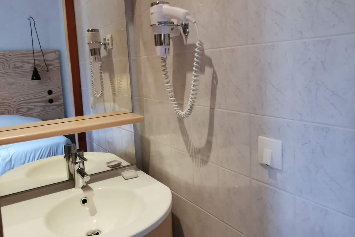 A bathroom with a sink, mirror, and a hairdryer mounted on the wall.
