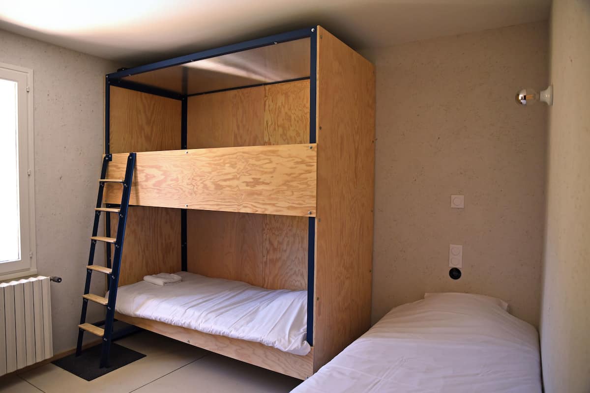 A bunk bed with a wooden frame and a ladder, a single bed to the right, and a radiator on the left.