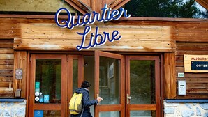 A wooden building with a sign reading "Quartier Libre" and a person entering through glass doors. - Hostel Quartier Libre (Saint-Jean-en-Royans)