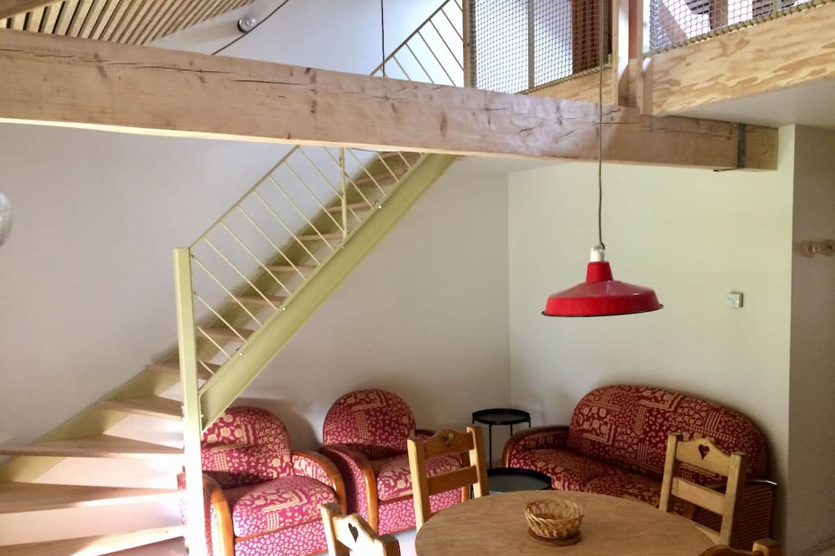 A room with a staircase, a round wooden table, and patterned sofas.