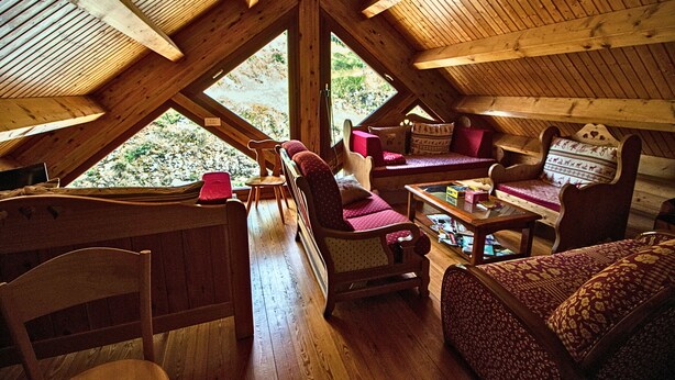A cozy attic room with wooden beams, a sofa, chairs, and a small table. - Hostel Quartier Libre (Saint-Jean-en-Royans)