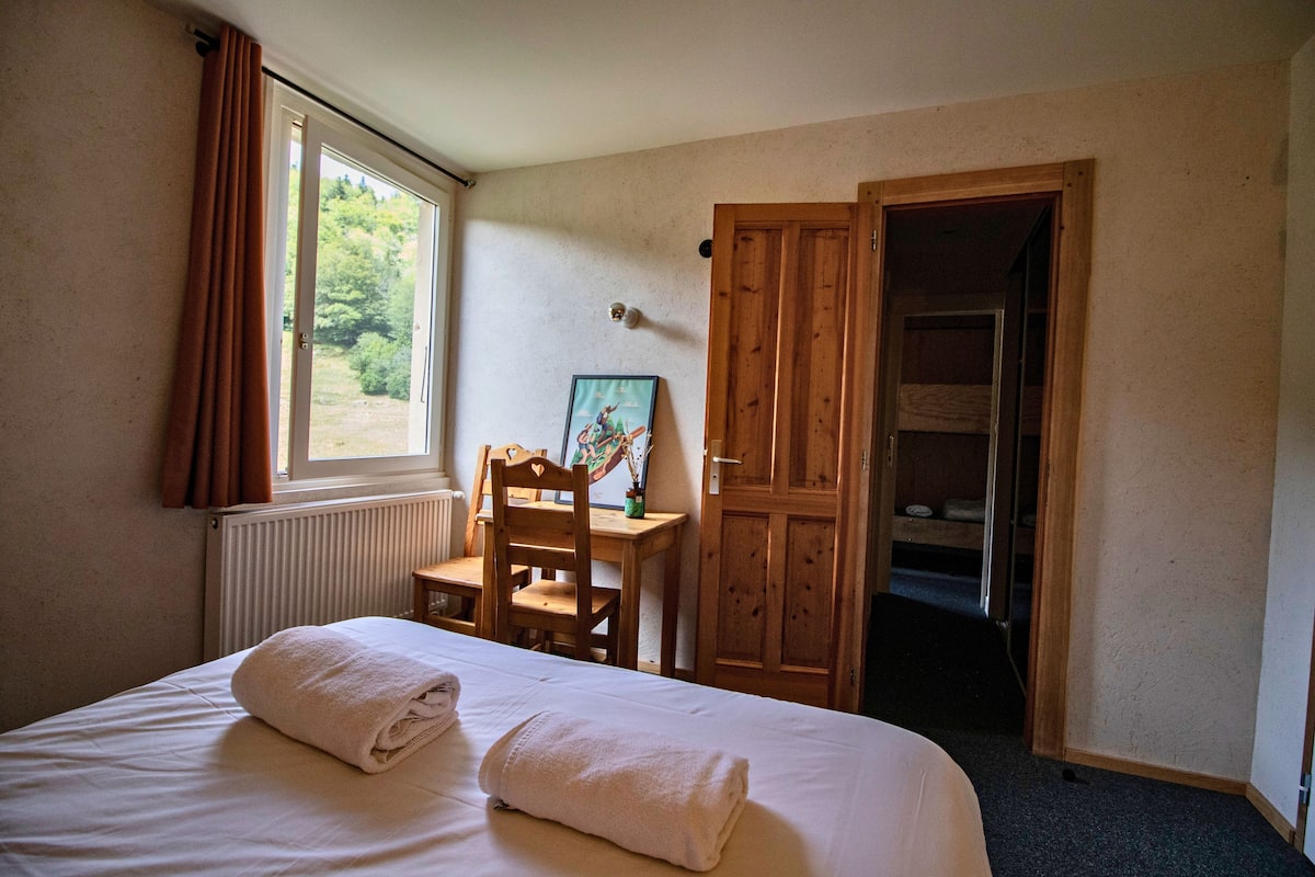 A hotel room with a bed, a wooden desk, a chair, and a wardrobe.