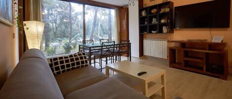 A living room with a sofa, a dining table with chairs, a TV, and a bookshelf.