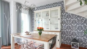 A dining area with a wooden table, clear chairs, a white cabinet with glass doors, and patterned wallpaper.
