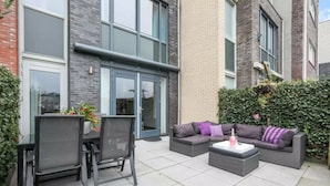 A patio area with a dining table and chairs, a sofa set, and a small table with a bottle.