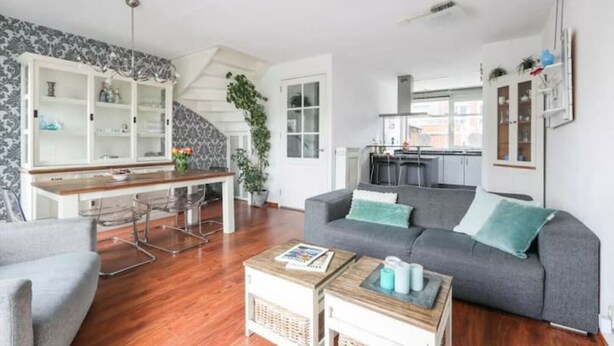 A modern living room with a grey sofa, wooden coffee table, and a dining area with a staircase.
