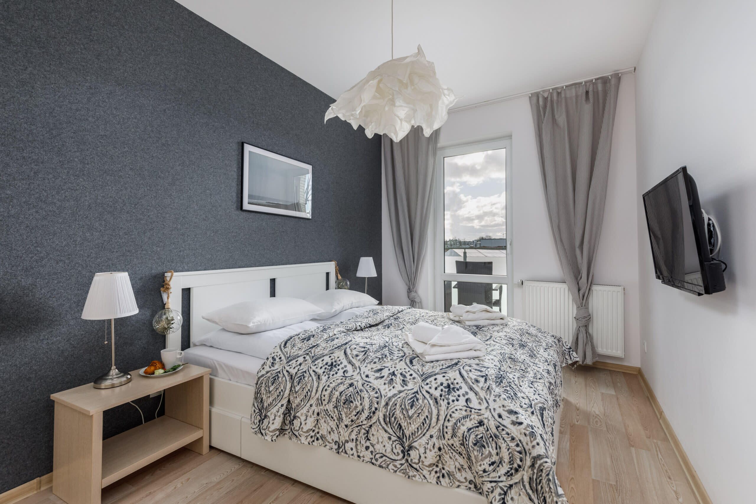 Une chambre à coucher avec un lit, des lampes de chevet, une table de chevet, un téléviseur et une fenêtre avec des rideaux.