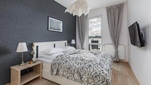Ein Schlafzimmer mit Bett, Nachttischlampen, einem Nachttisch, einem Fernseher und einem Fenster mit Vorhängen.