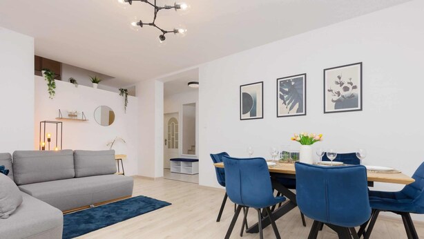 A modern living room with a grey sofa, blue chairs, and a dining table set for four.