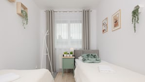 A bedroom with two beds, a bedside table with a lamp, and a window with curtains.