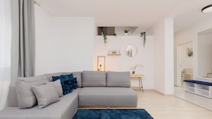 A modern living room with a grey sectional sofa, a blue rug, and a small desk with a mirror and plants.