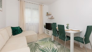 A modern living room with a sofa, a dining table with chairs, a TV, and a window with curtains.