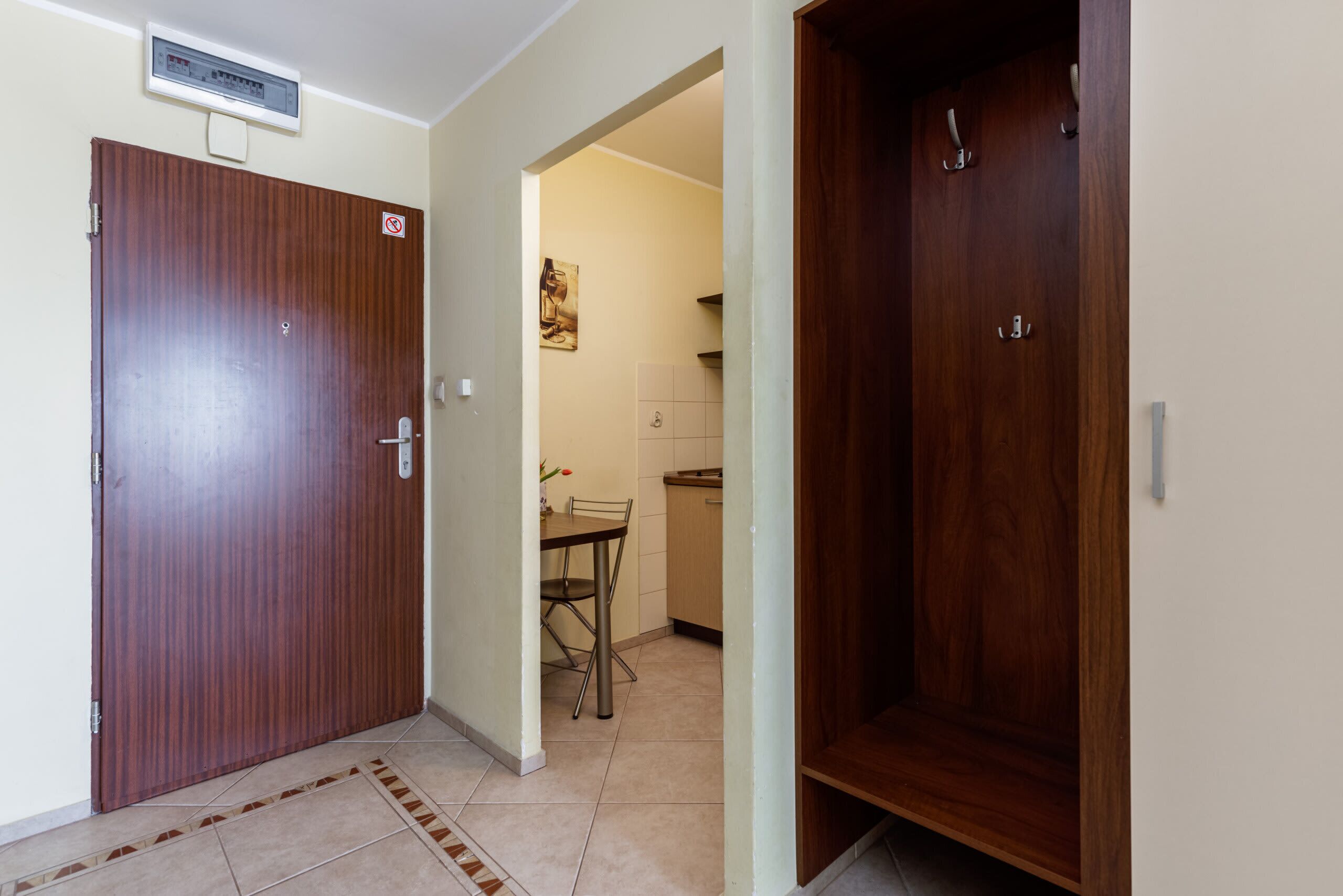 Un couloir avec deux portes en bois, un sol carrelé et une petite table avec une chaise.