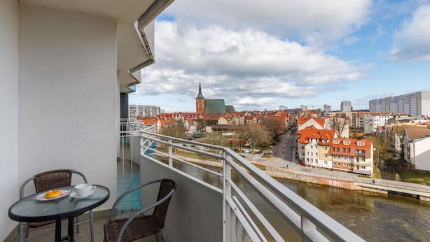 Ein Balkon mit Tisch und Stühlen mit Blick auf eine Stadtlandschaft, inklusive Fluss und Gebäuden.